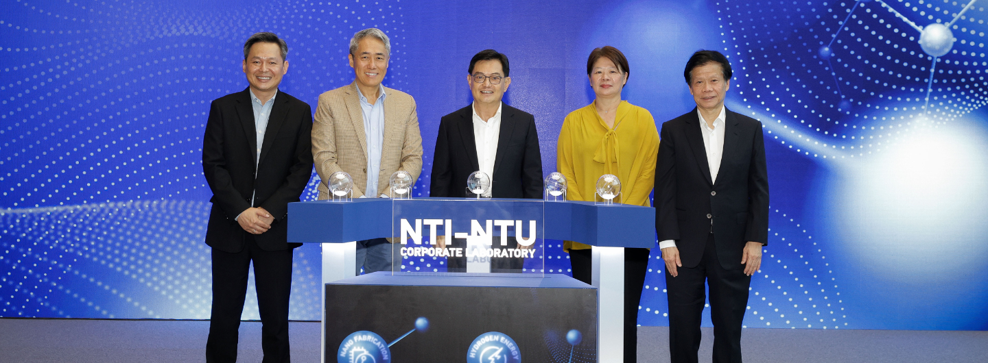 Five adults standing behind a blue NTI-NTU Corporate Laboratory podium with crystal globe awards.
